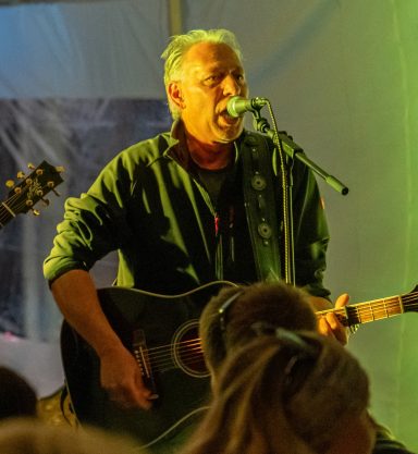 Mann spielt akustische Gitarre und singt auf einer Bühne vor Publikum.