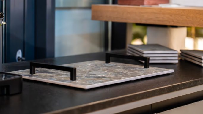 Beige Platte mit schwarzen Griffen auf einem eleganten Tisch, im Hintergrund Stapel von Heften.