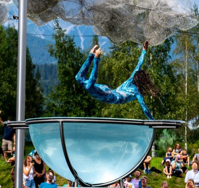 Akrobatin springt aus einer Glasschale, umgeben von Zuschauern und Natur.