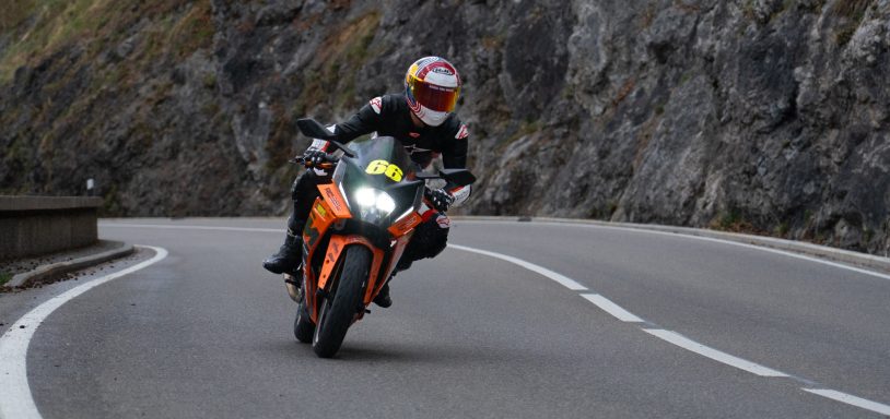 Motorradfahrer in Schutzkleidung fährt kurvenreiche Straße entlang.