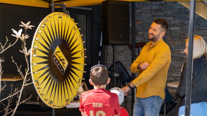Mann und Kind stehen vor einem Glücksrad unter einem Zelt.