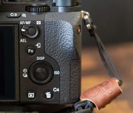 Nahaufnahme einer Kamera mit Fokus auf dem Bedienfeld und einem Lederriemen.