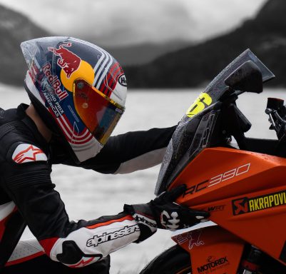 Motorradfahrer in Schwarz-Weiß-Outfit und Helm, konzentriert auf sein orangefarbenes Motorrad.