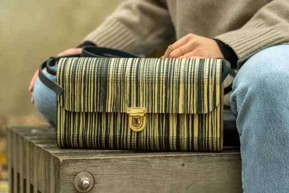 Beige und schwarze gestreifte Handtasche auf einer Bank, zusammen mit einer Person.