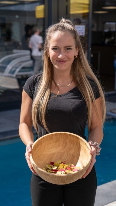 Lächelnde Frau mit langen Haaren hält eine Holzschale mit Blumenblättern.