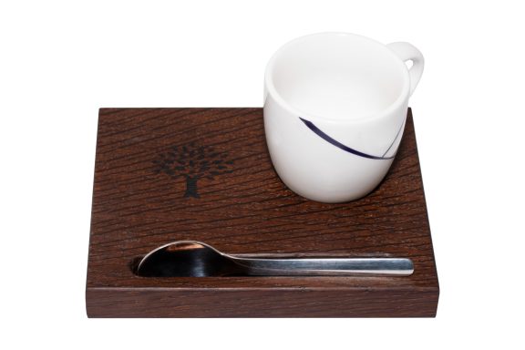 Weiße Tasse mit Löffel auf einem Holzuntersetzer mit Baum-Motiv.