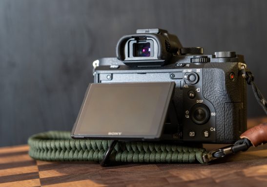 Spiegelreflexkamera mit einem Monitor und Kamera-Gurt auf einem Holztisch.